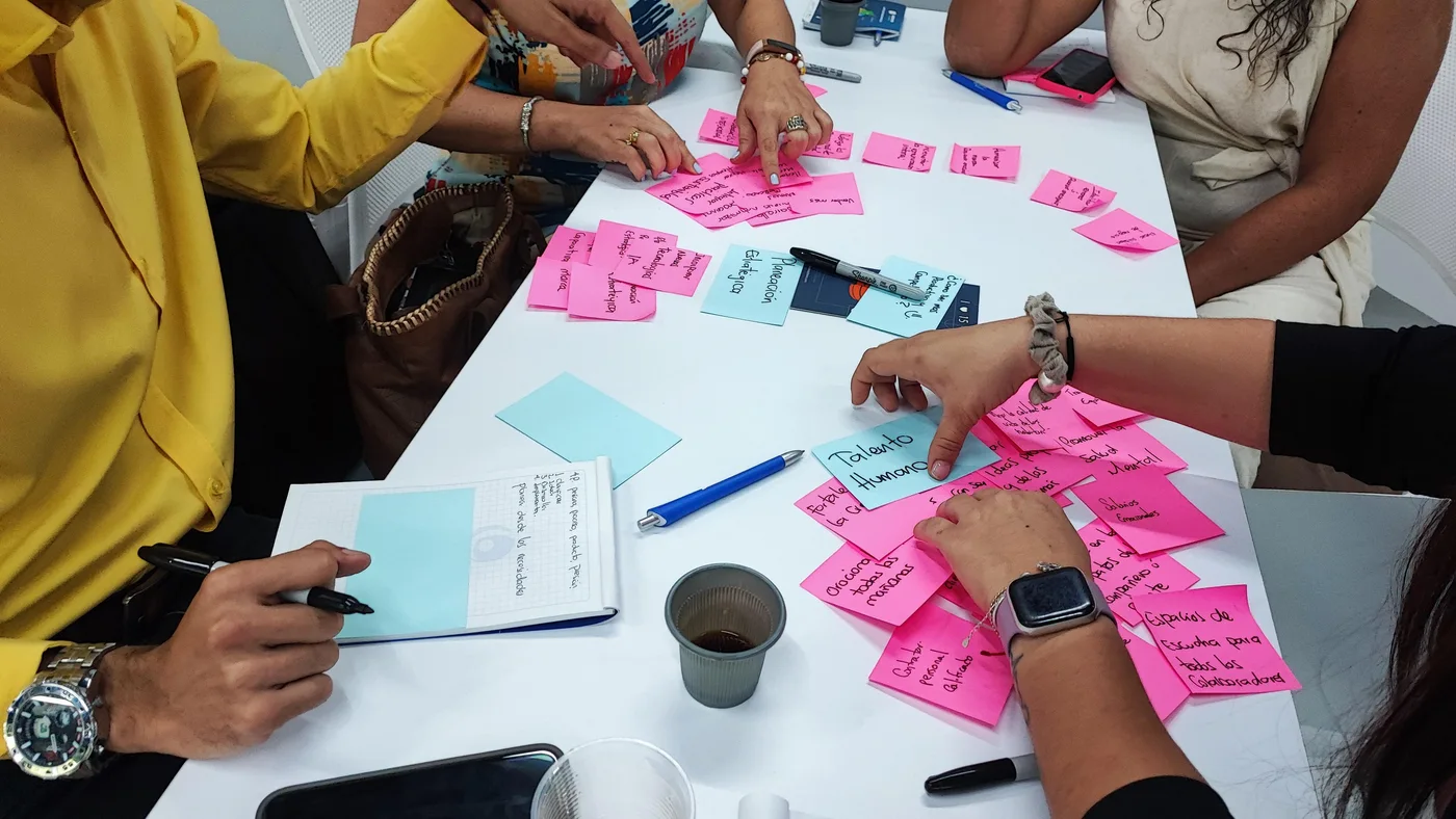 Participantes de un taller construyen ideas juntos con notas adhesivas sobre una mesa